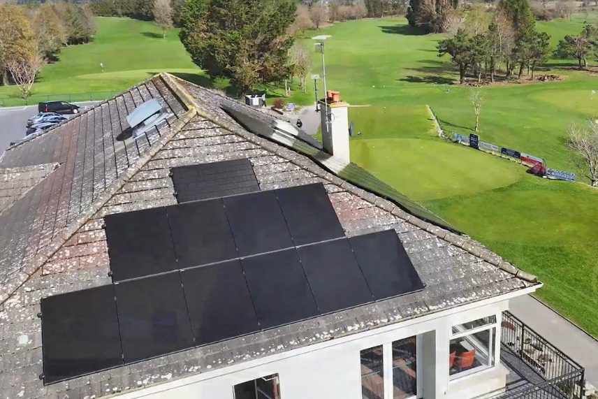 Golf Club Solar Panel Installation Clubhouse Roof Image showing 28 solar panels on the roof in the foreground and the golf course in the background.