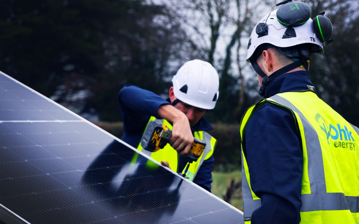 How Many Solar Panels Are Needed To Run A Home In Northern Ireland Featured Image showing Ohk energy electricians working on solar panels in a garden.