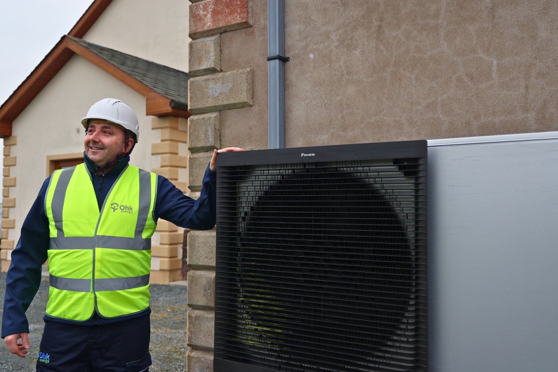 Air to Water Heat Pumps vs Other Heating Systems Image of an Ohk energy air to water heat pump installer standing next to a heat pump he installed.