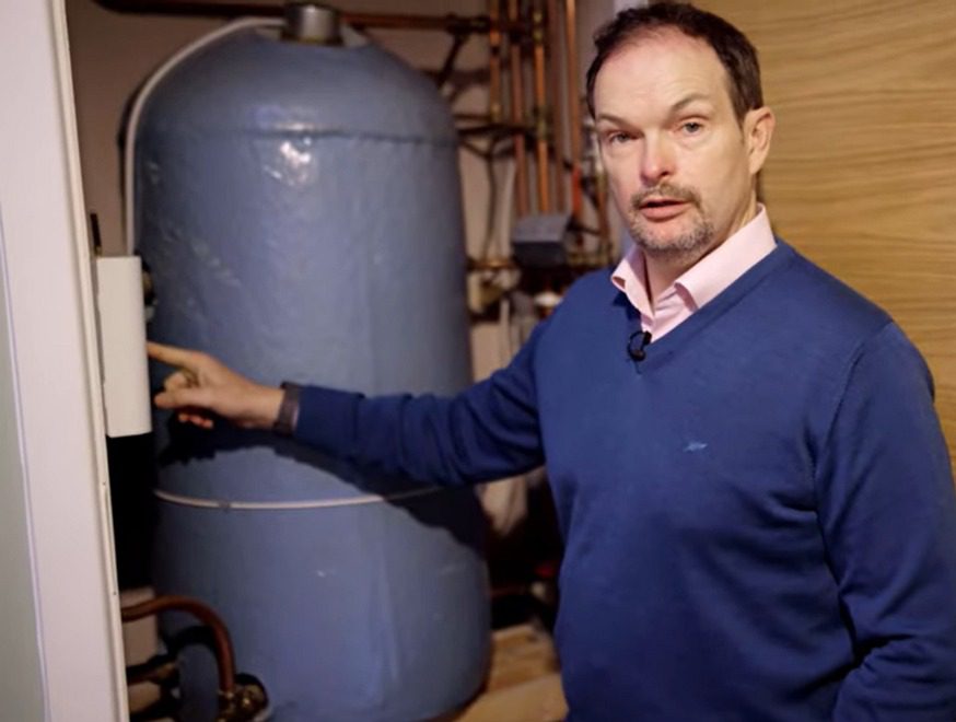 Hot Water Diverter eddi Installation Video Preview Image showing an Ohk energy customer in his home pointing to his eddi solar diverter.