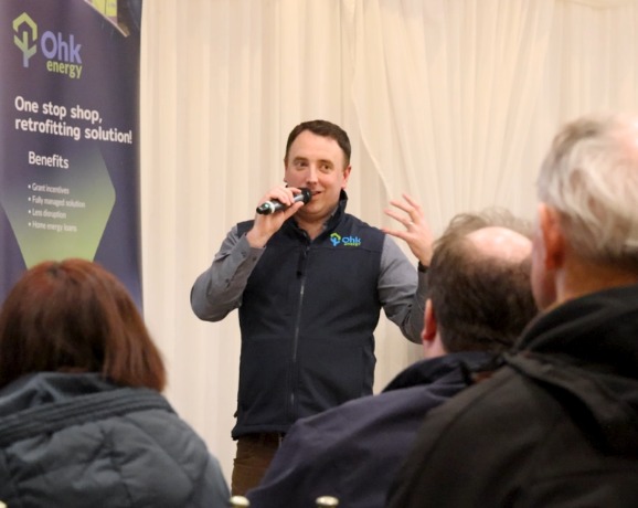 Local One Stop Shop Information Evening image showing an Ohk energy representative, beside a One Stop Shop pull up stand, speaking to an audience.
