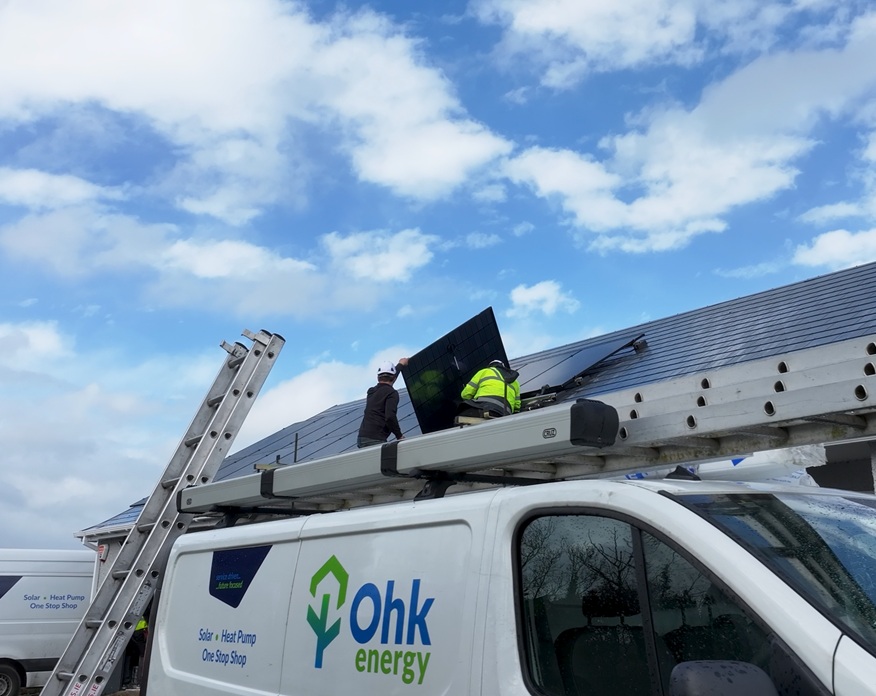 Installing Solar Panels Image showing Ohk energy solar panel installers on a roof mounting modules, with an Ohk energy van in the foreground