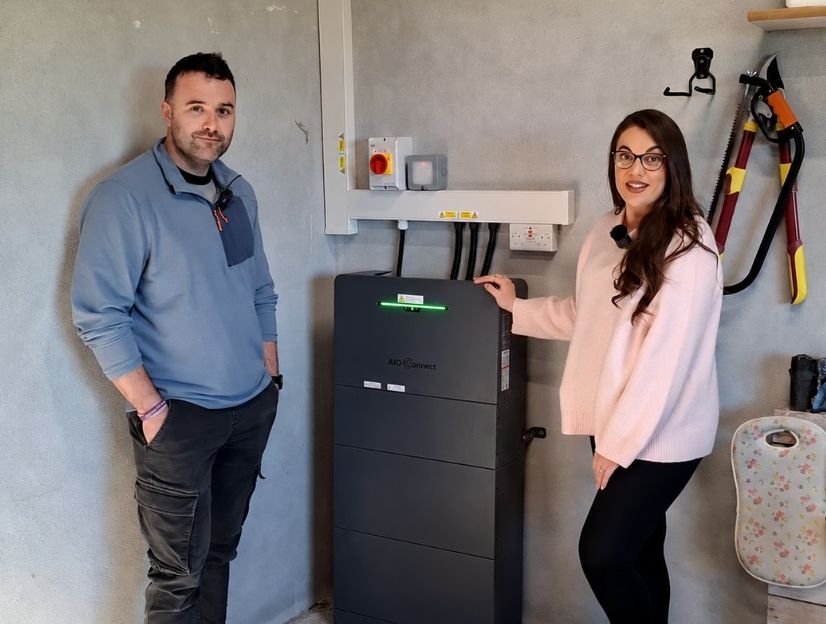 AiO Konnect Installation image showing Ohk energy customers standing beside an AiO Konnect unit installed in a garage.